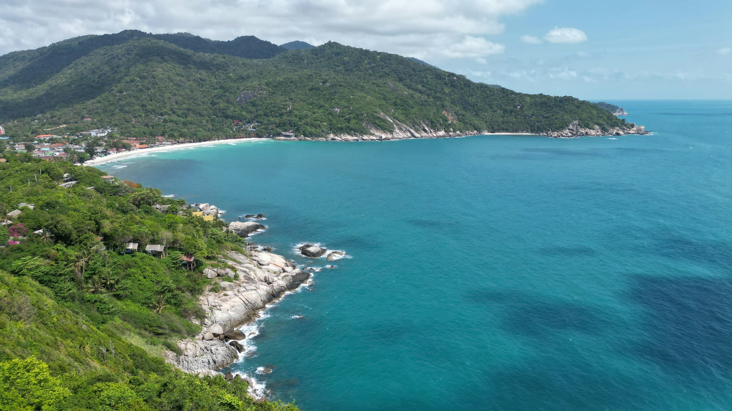 Aerial view of a curved Koh Samui bay framed by tropical hills and rocky coastline